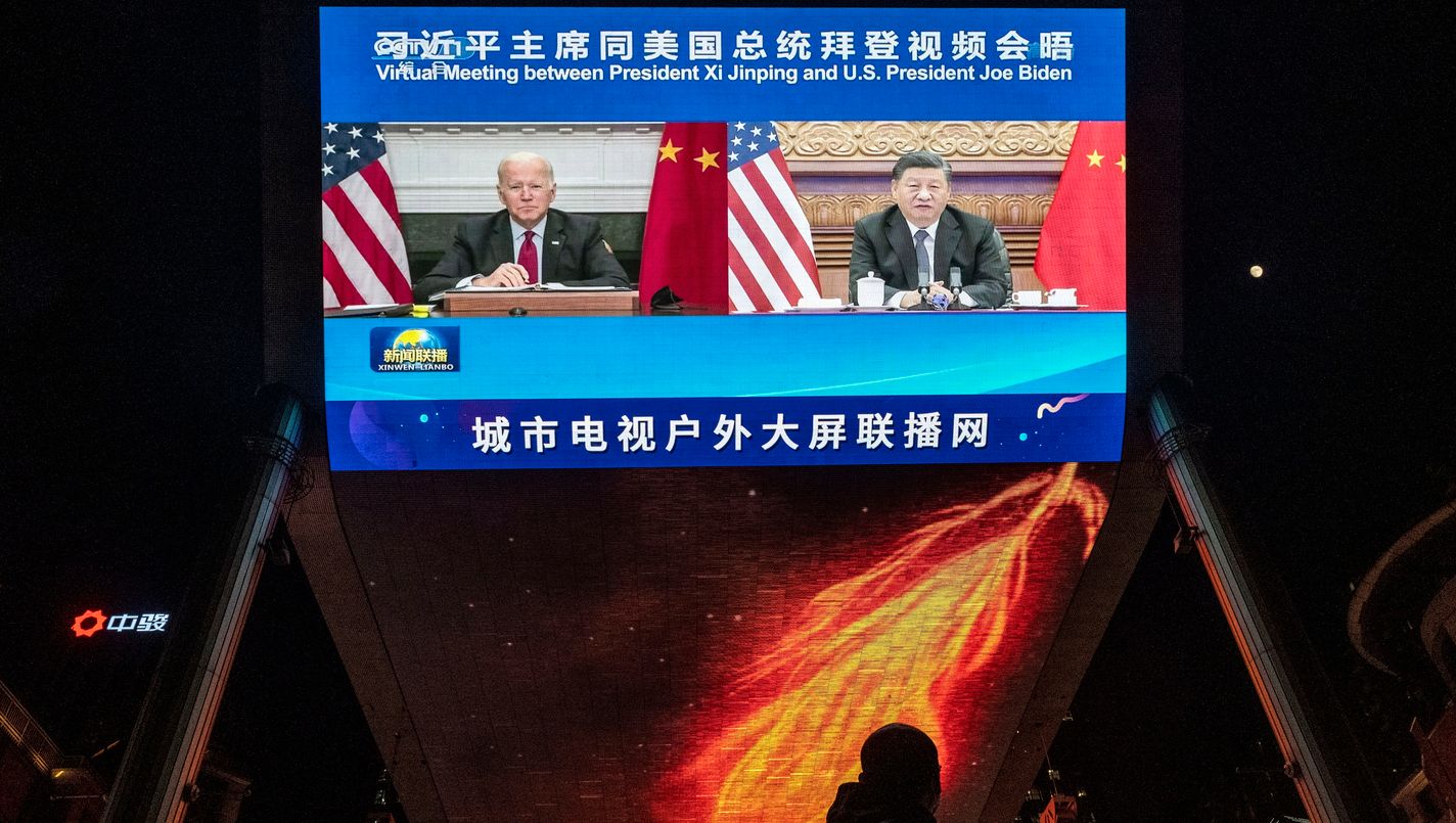 A large screen displays United States President Joe Biden, left, and China's President Xi Jinping during a virtual summit as people walk by during the evening CCTV news broadcast outside a shopping mall in Beijing, China.