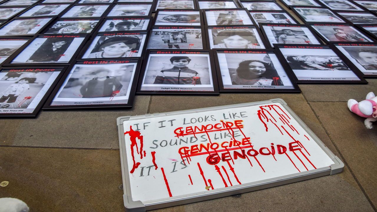 A placard with a description of genocide is seen next to pictures of children killed in Gaza placed by protesters.